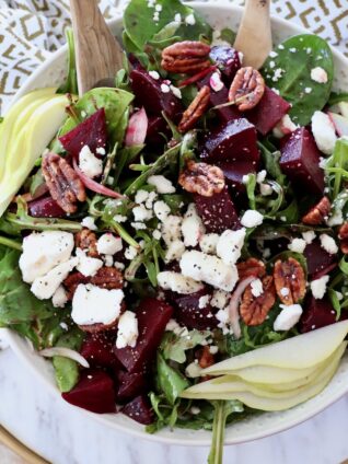 salad in bowl with serving spoons topped with roasted beets and feta cheese