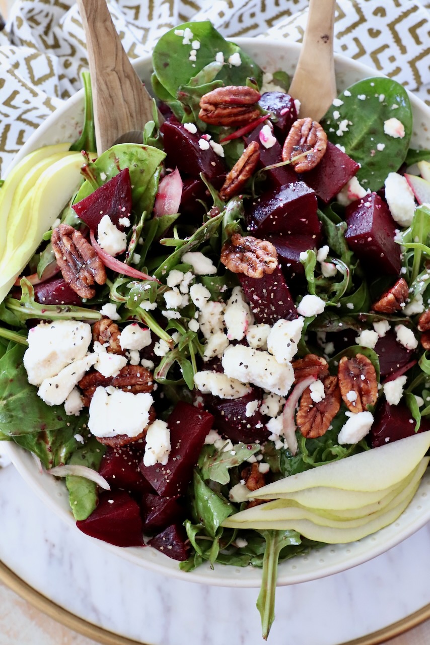 salad in bowl with serving spoons topped with roasted beets and feta cheese