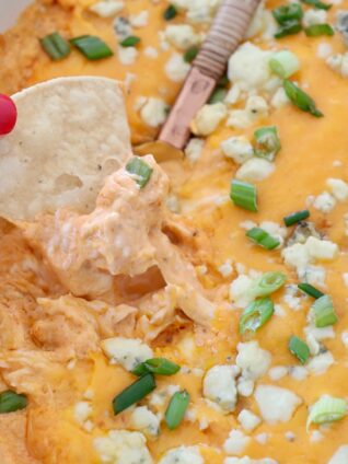 hand lifting chip out of buffalo chicken dip in baking dish