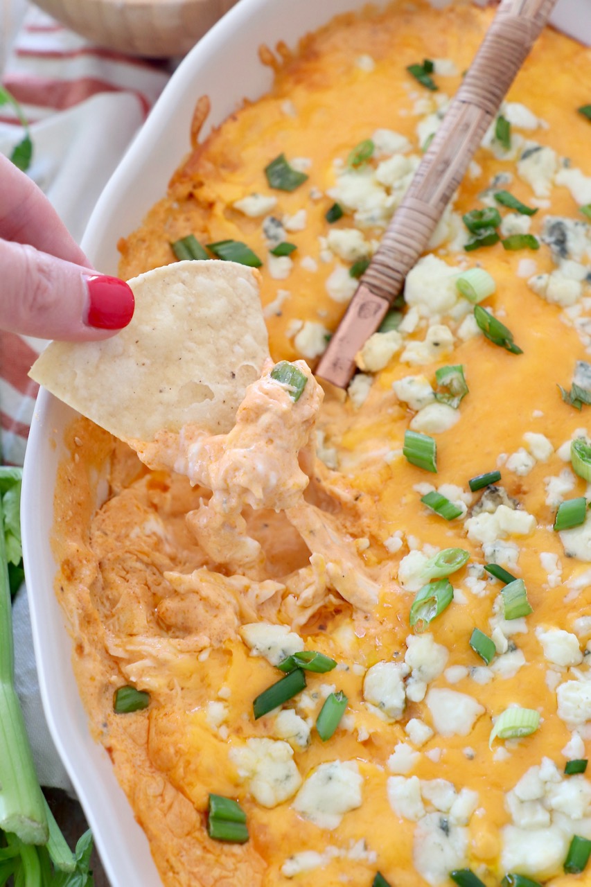 hand lifting chip out of buffalo chicken dip in baking dish