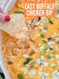 hand lifting chip out of buffalo chicken dip in baking dish