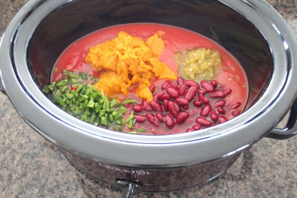 slow cooker filled with tomatoes, pumpkin purée, jalapeños, chilies, and kidney beans.