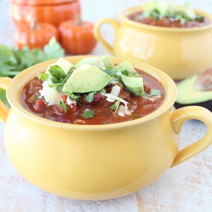 Yellow bowl filled with Pumpkin Chili garnished with melted cheese, avocado, and cilantro.