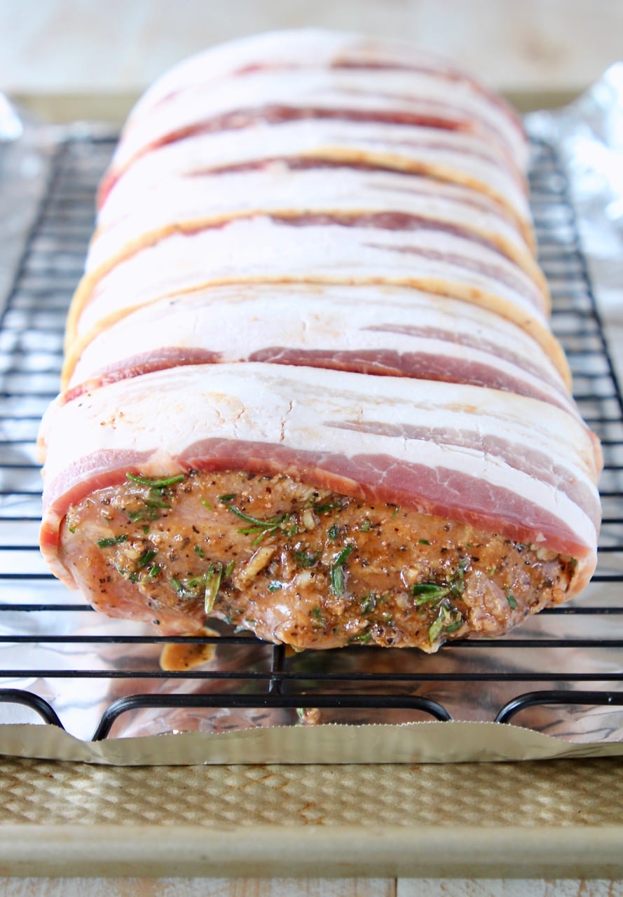 Bacon wrapped herb and balsamic pork loin uncooked on wire rack on top of foil lined baking sheet