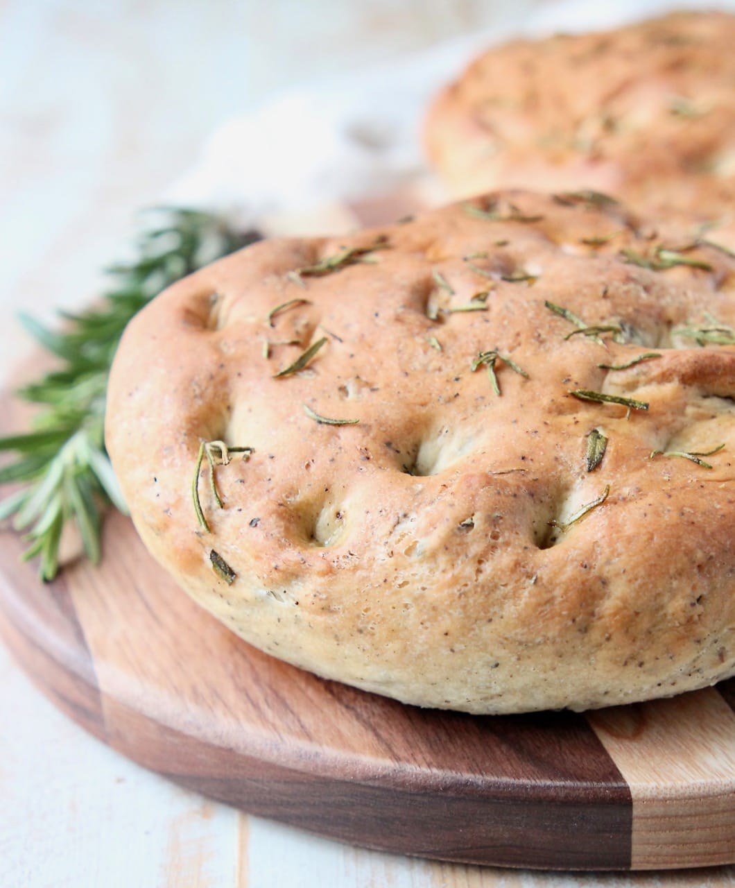 Rosemary focaccia bread on wood cutting board with fresh rosemary sprigs