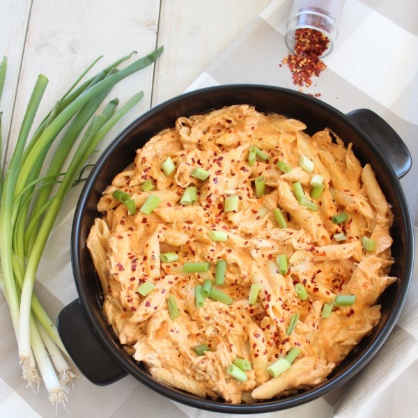 Buffalo Chicken Pasta with creamy cheesy sauce in baking dish with green onions and red pepper flakes