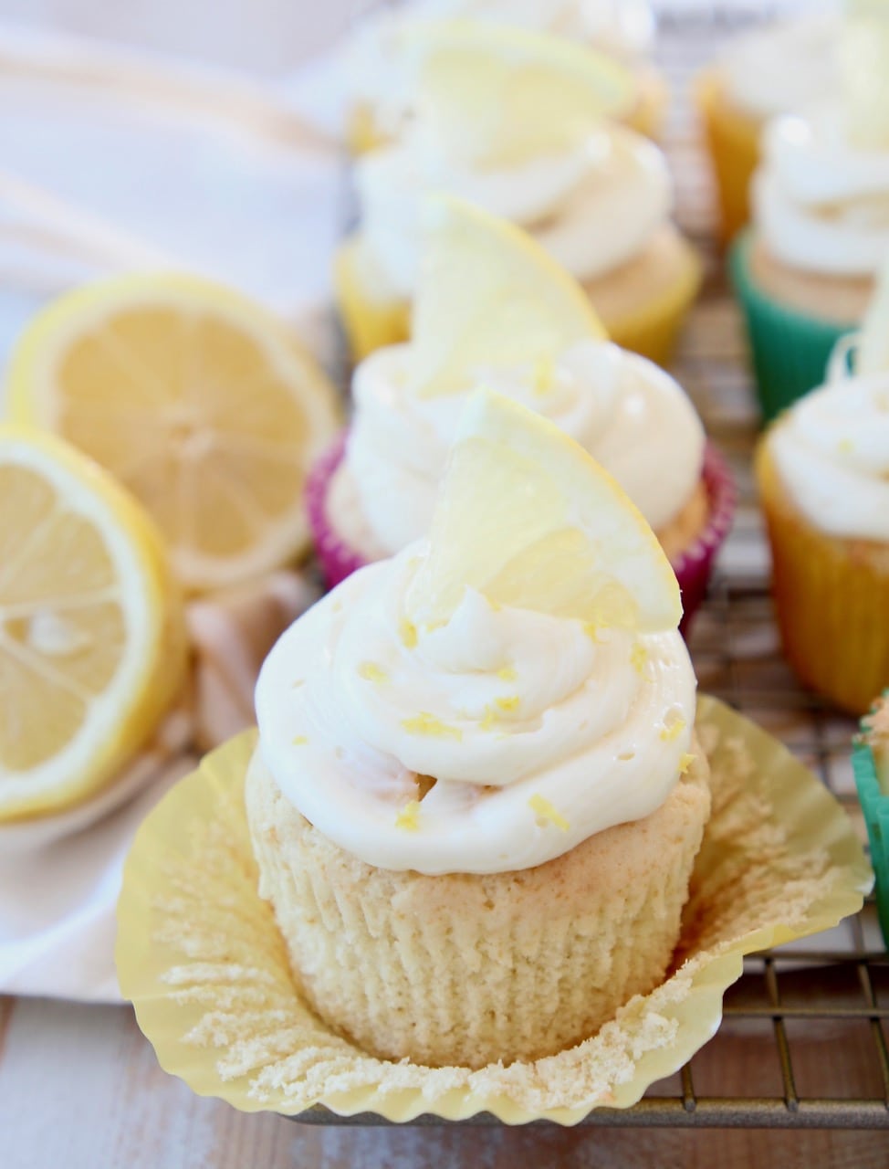 Lemon cupcake with wrapper unfolded, topped with lemon cream cheese frosting and lemon wedge