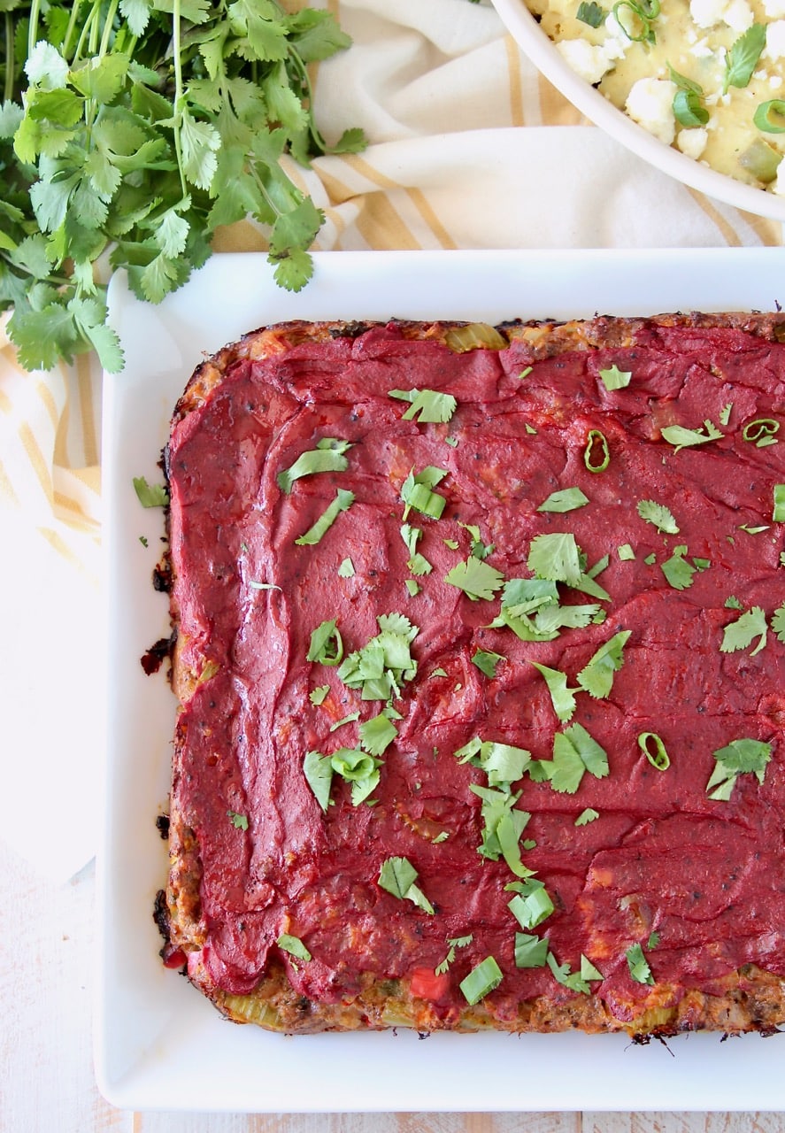 Cooked Mexican meatloaf on white plate topped with tomato paste and cilantro