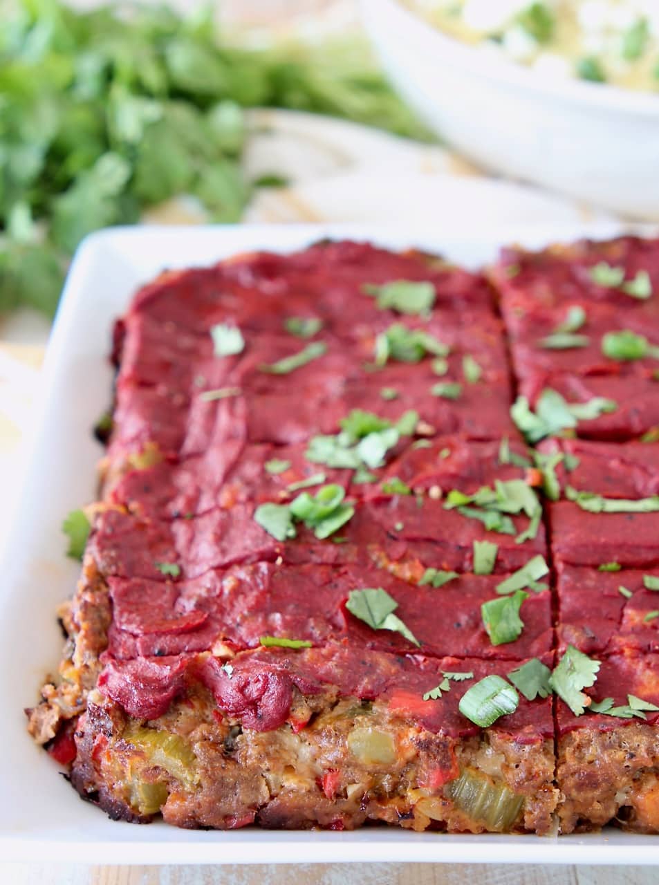Mexican meatloaf topped with tomato paste, sliced on a white plate with fresh cilantro