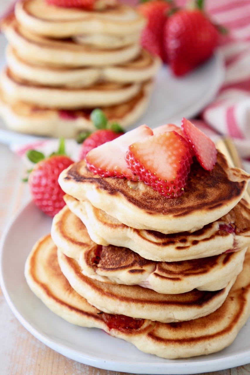 Strawberry pancakes stacked up on plate with fresh strawberries