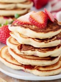 Strawberry pancakes stacked on plate with fresh strawberry slices