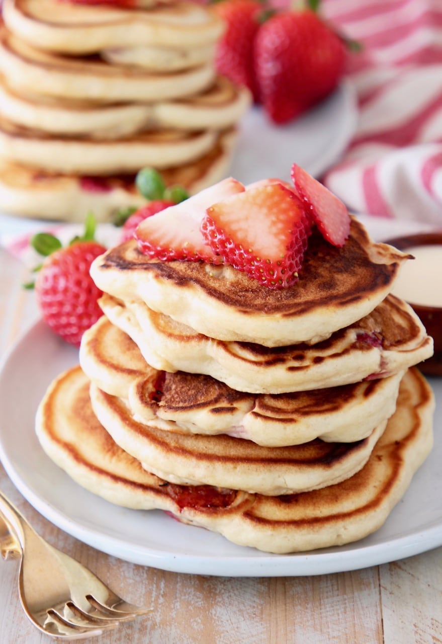 Strawberry pancakes stacked up on a plate topped with fresh strawberry slices