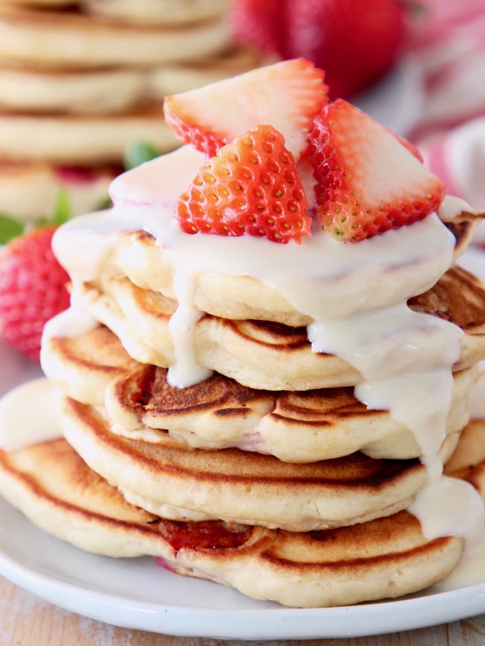 Strawberry pancakes stacked up on a plate topped with cream cheese syrup and fresh strawberry slices