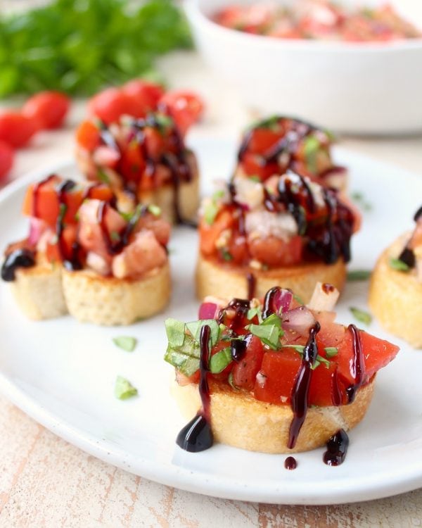 pieces of tomato bruschetta on plate drizzled with balsamic reduction