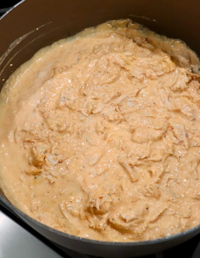 creamy sauce tossed with cooked, shredded chicken in pot