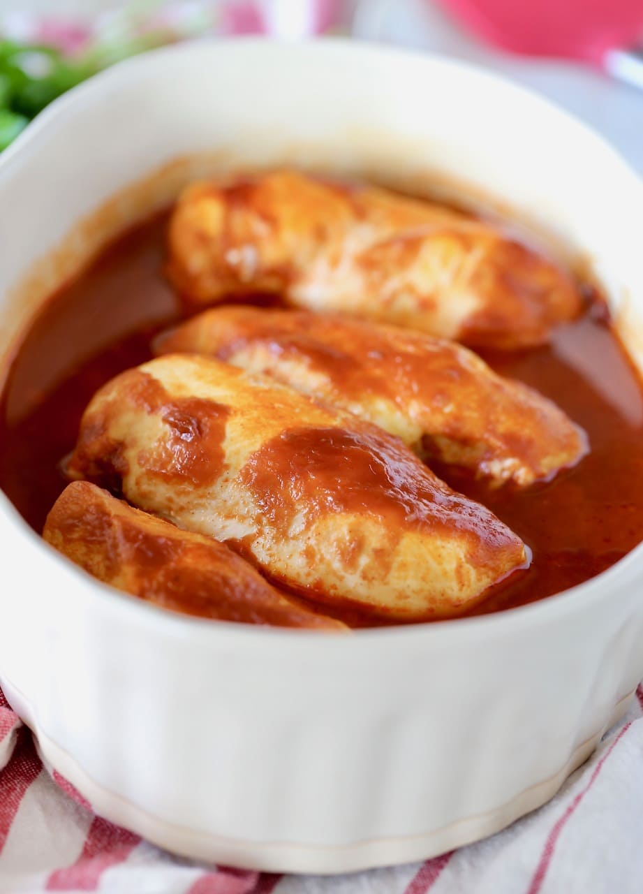 Baked BBQ Buffalo Chicken in oval casserole dish on top of red and white striped towel