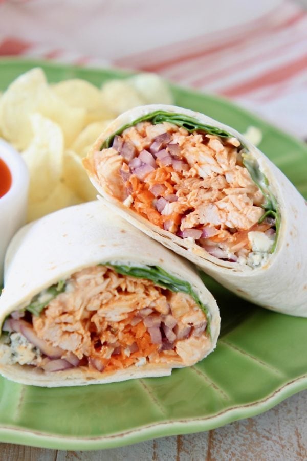 Buffalo chicken wrap cut in half and leaning on each other on green plate with potato chips