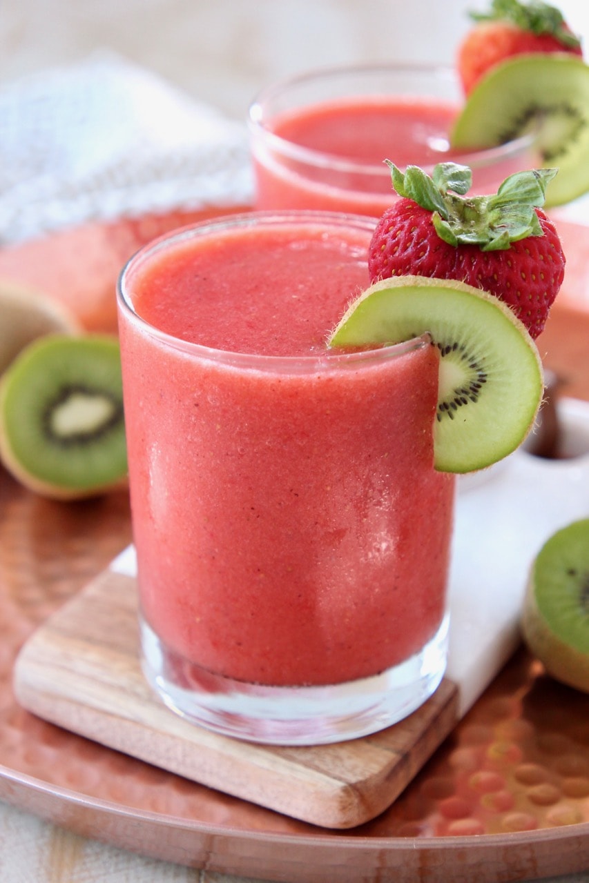 Strawberry slushie in glass with strawberry and kiwi slice on the rim of the glass