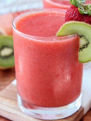 Strawberry slush in glass with kiwi slice and strawberry on the rim of the glass