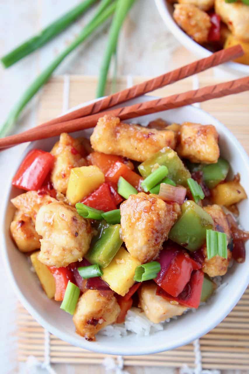 Sweet and sour chicken in bowl with chopsticks and green onions