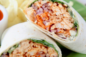 Buffalo chicken wrap sliced in half on green plate with potato chips