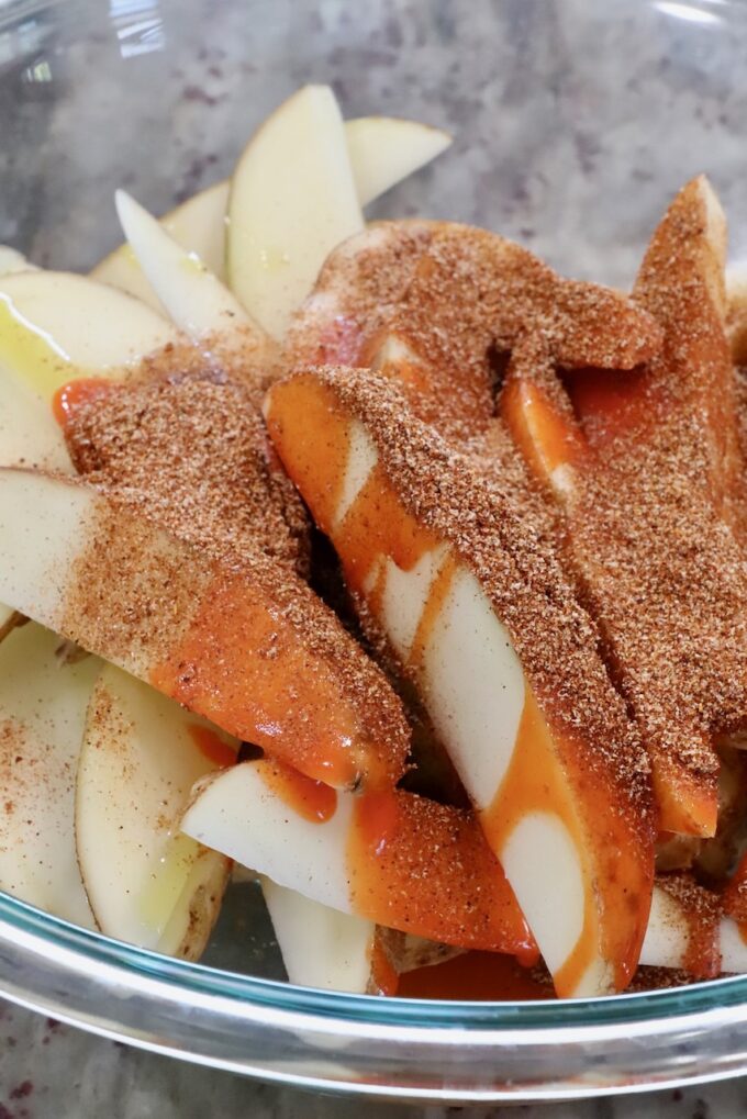 potato slices in a glass bowl are covered with seasonings and hot sauce