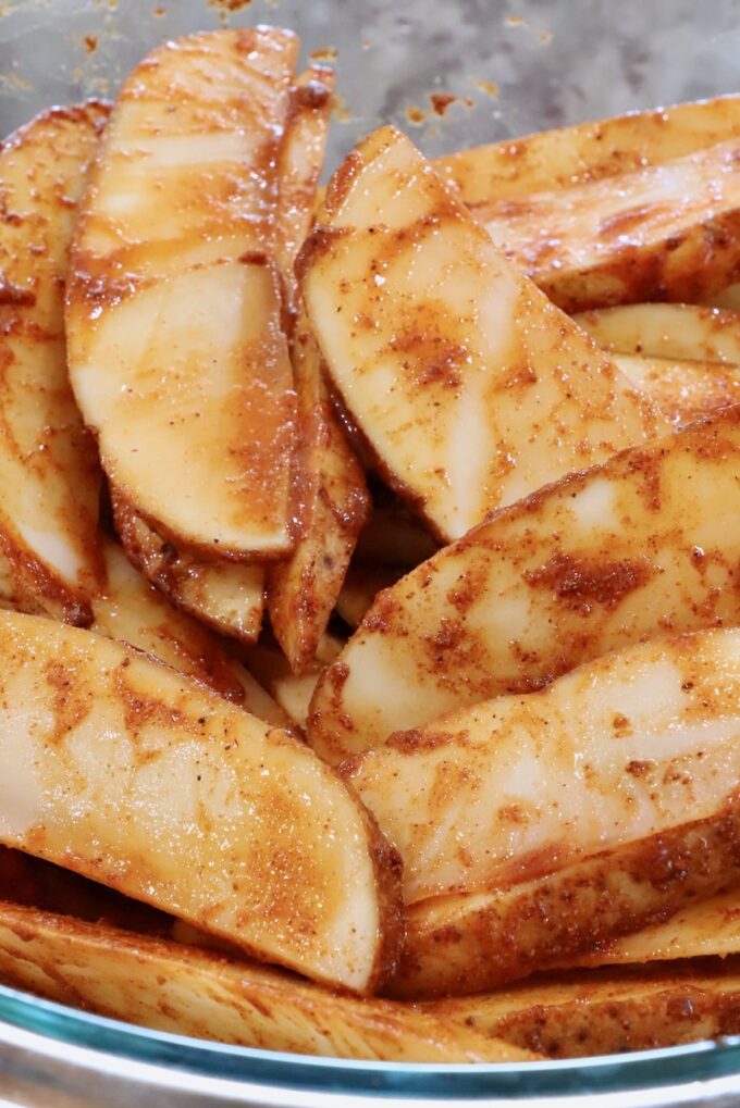 Close-up image of sliced potatoes coated with seasonings and hot sauce, arranged in a bowl.