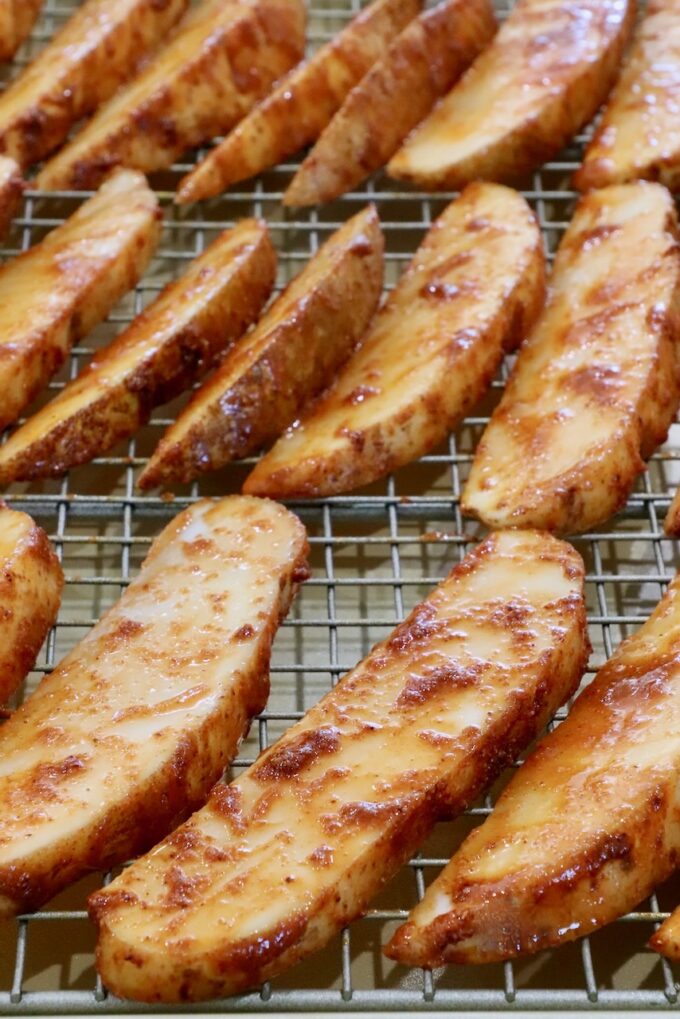 Close-up image of sliced potatoes coated with seasonings and hot sauce, arranged on a wire rack over a baking sheet