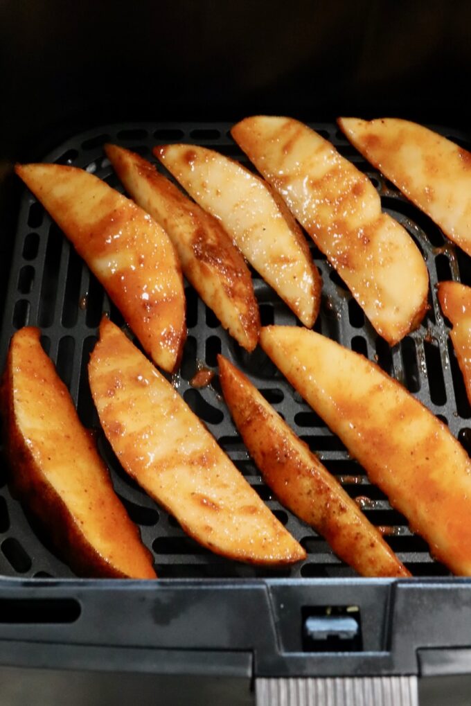 sliced potatoes coated with seasonings and hot sauce, arranged in an air fryer basket