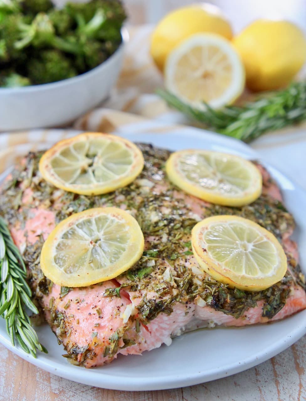 Piece of baked salmon on plate, topped with herbs and lemon slices
