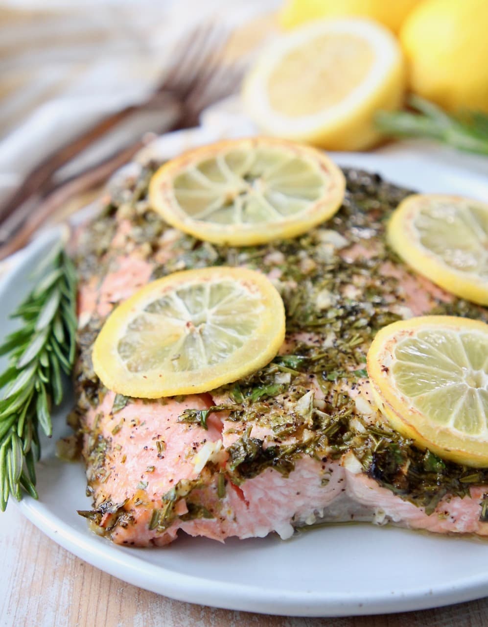 Herb roasted salmon on plate with lemon slices and a rosemary sprig on the side
