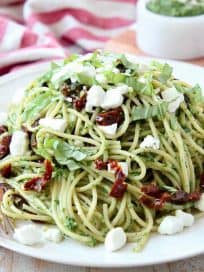 Pesto spaghetti on plate with goat cheese crumbles on top and gold fork on the side