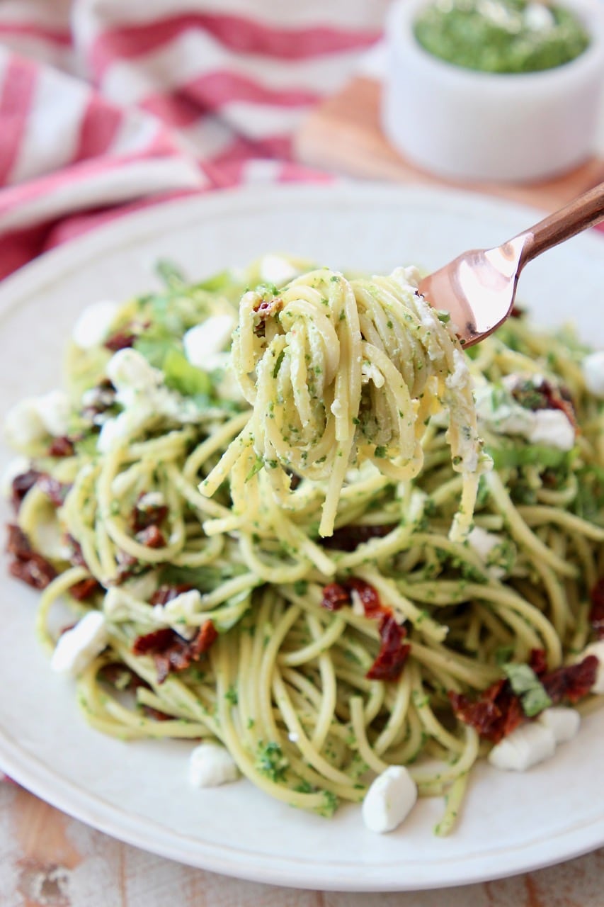 Pesto spaghetti on plate, with fork twirling the spaghetti lifted over the plate
