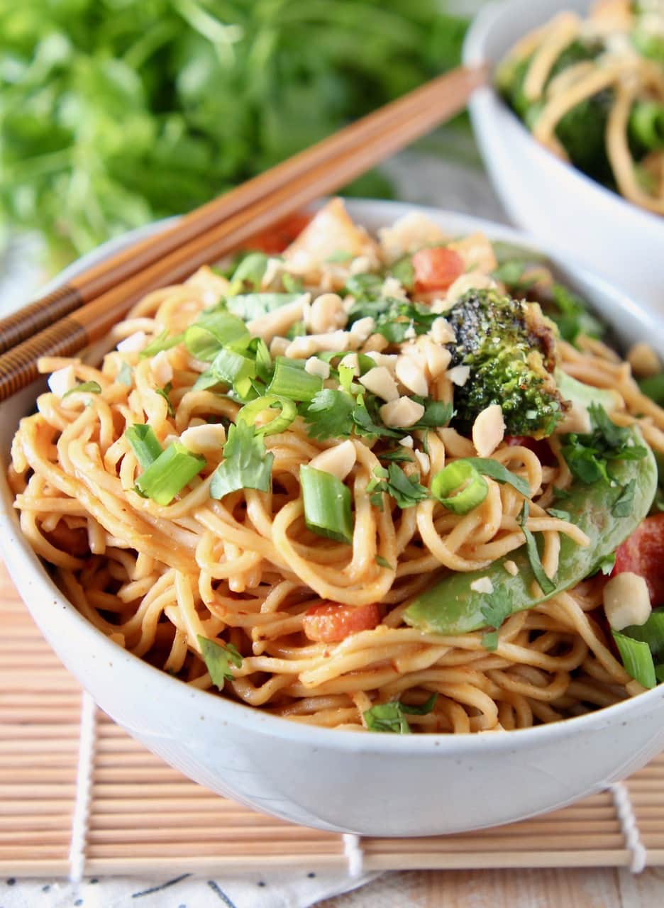 Vegetables and noodles in bowl, topped with green onions and peanuts, with chopsticks on the side of the bowl