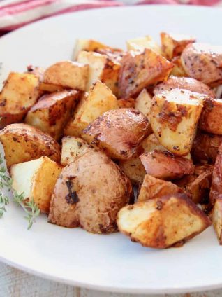 Crispy baked Cajun red potatoes on white plate with fresh thyme sprigs