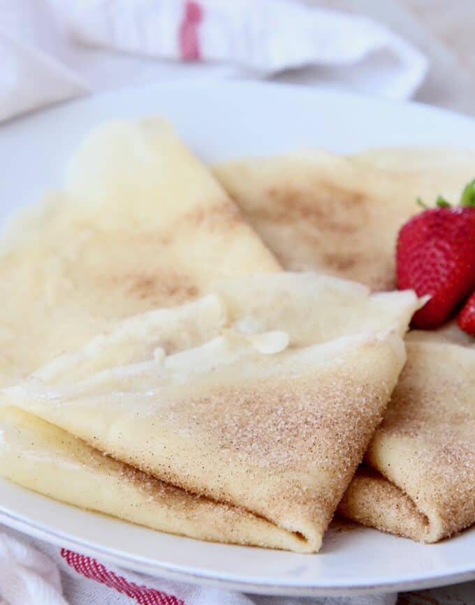 cinnamon sugar crepes folded on plate with strawberries