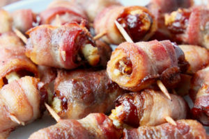 Bacon wrapped dates on plate on top of wood cutting board
