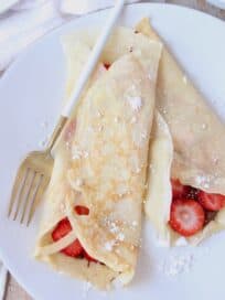 Crepes rolled up on plate filled with nutella and sliced strawberries