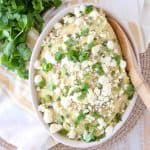 Mashed potatoes in a bowl with a wooden spoon, topped with queso fresco and fresh cilantro