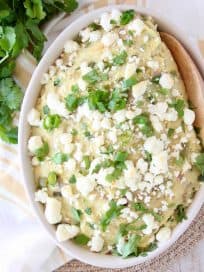 Mashed potatoes in a bowl with a wooden spoon, topped with queso fresco and fresh cilantro
