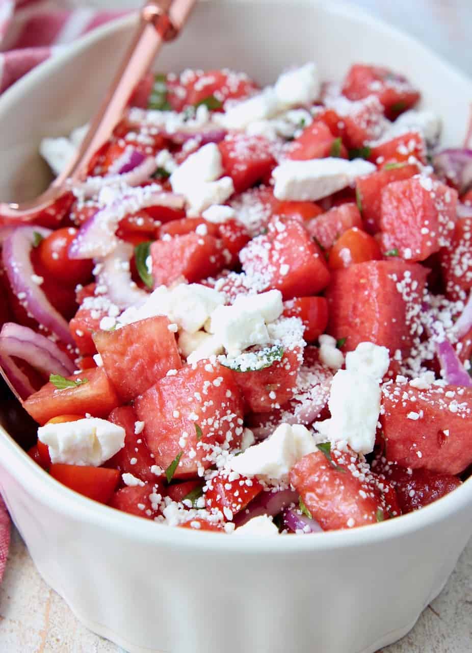 Diced watermelon with feta cheese and sliced onions in bowl with spoon