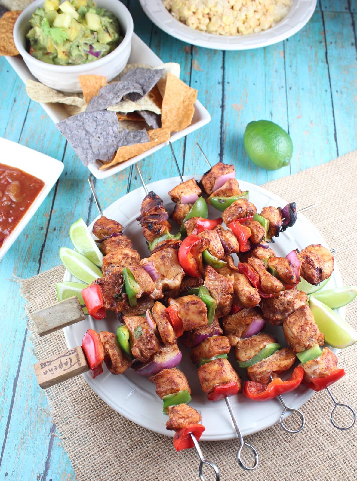 Chicken fajita skewers on plate with lime wedges, with chips and salsa on the side