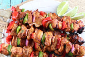 Grilled fajita chicken skewers on plate with lime wedges