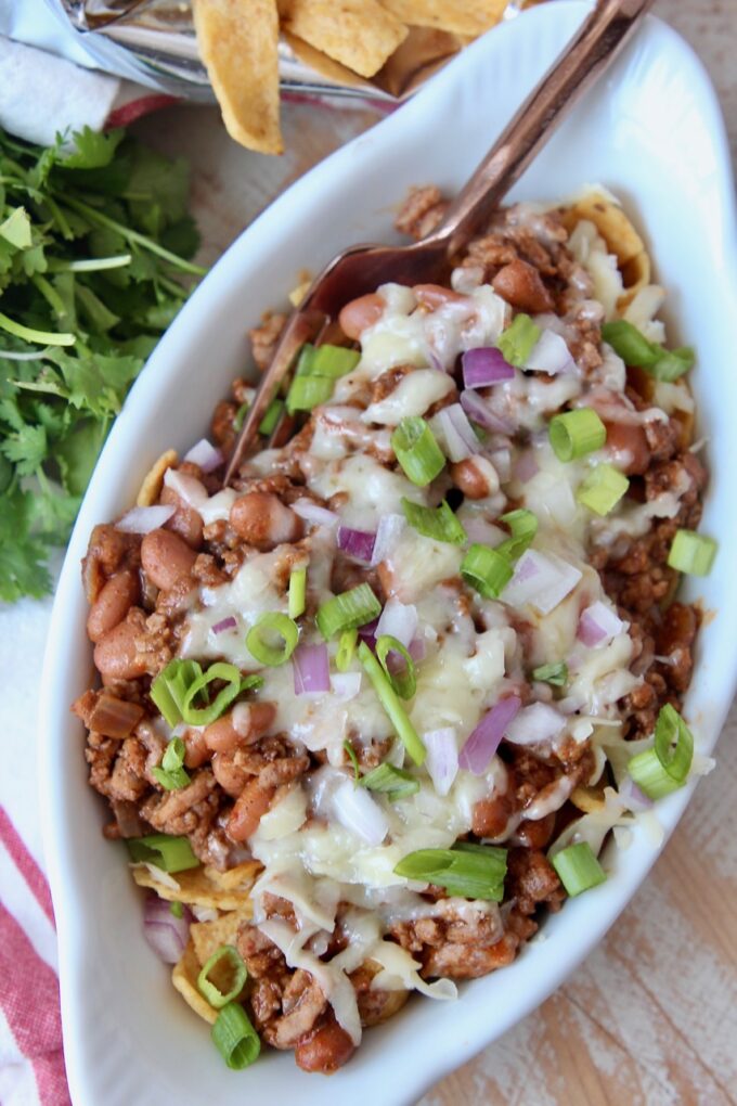 frito chili pie in white oval bowl topped with diced green onions