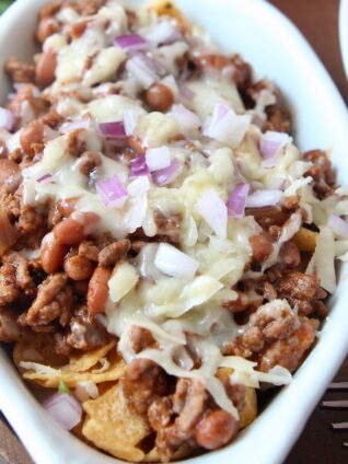 frito chili pie topped with cheese and diced red onion