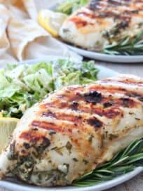 grilled chicken breast on plate with rosemary sprigs and lemon wedges