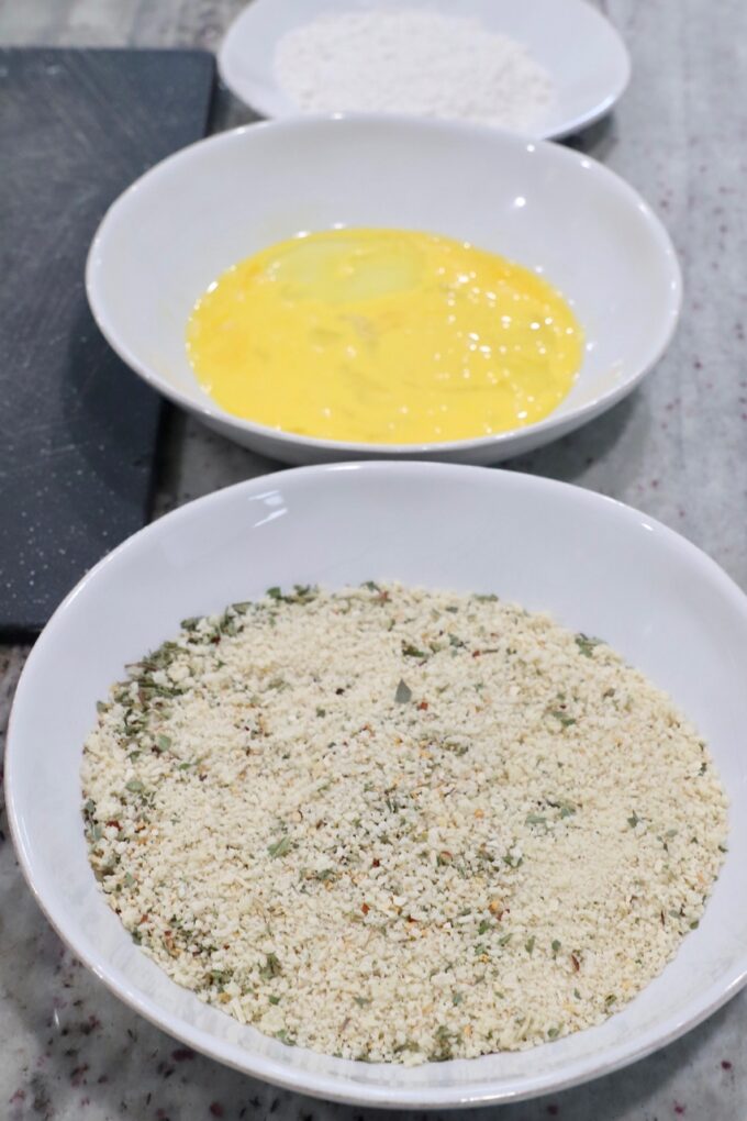 three bowls, filled with breadcrumbs, whisked eggs and flour