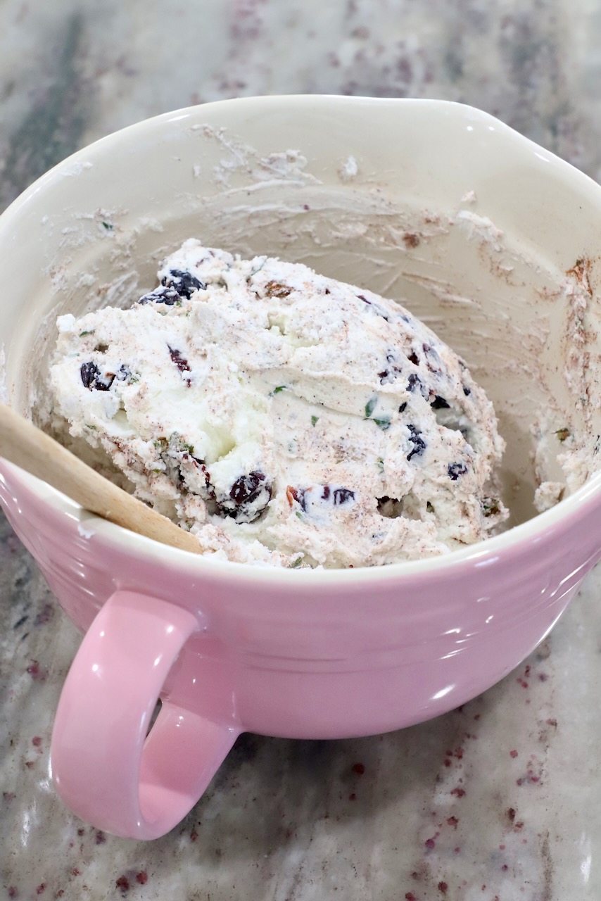 goat cheese combined with dried cranberries and rosemary in a pink mixing bowl