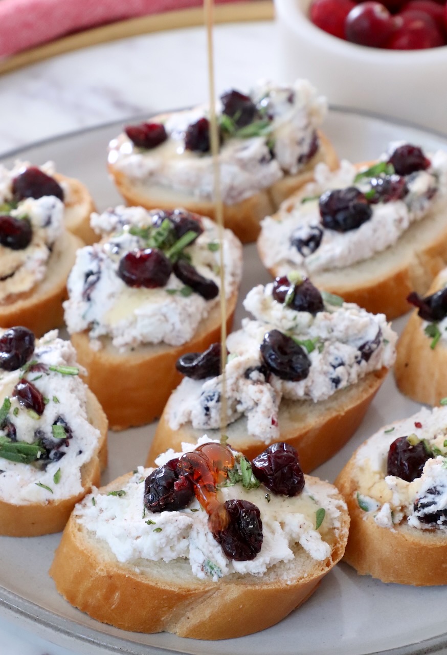 honey drizzling over cranberry goat cheese crostini on a plate