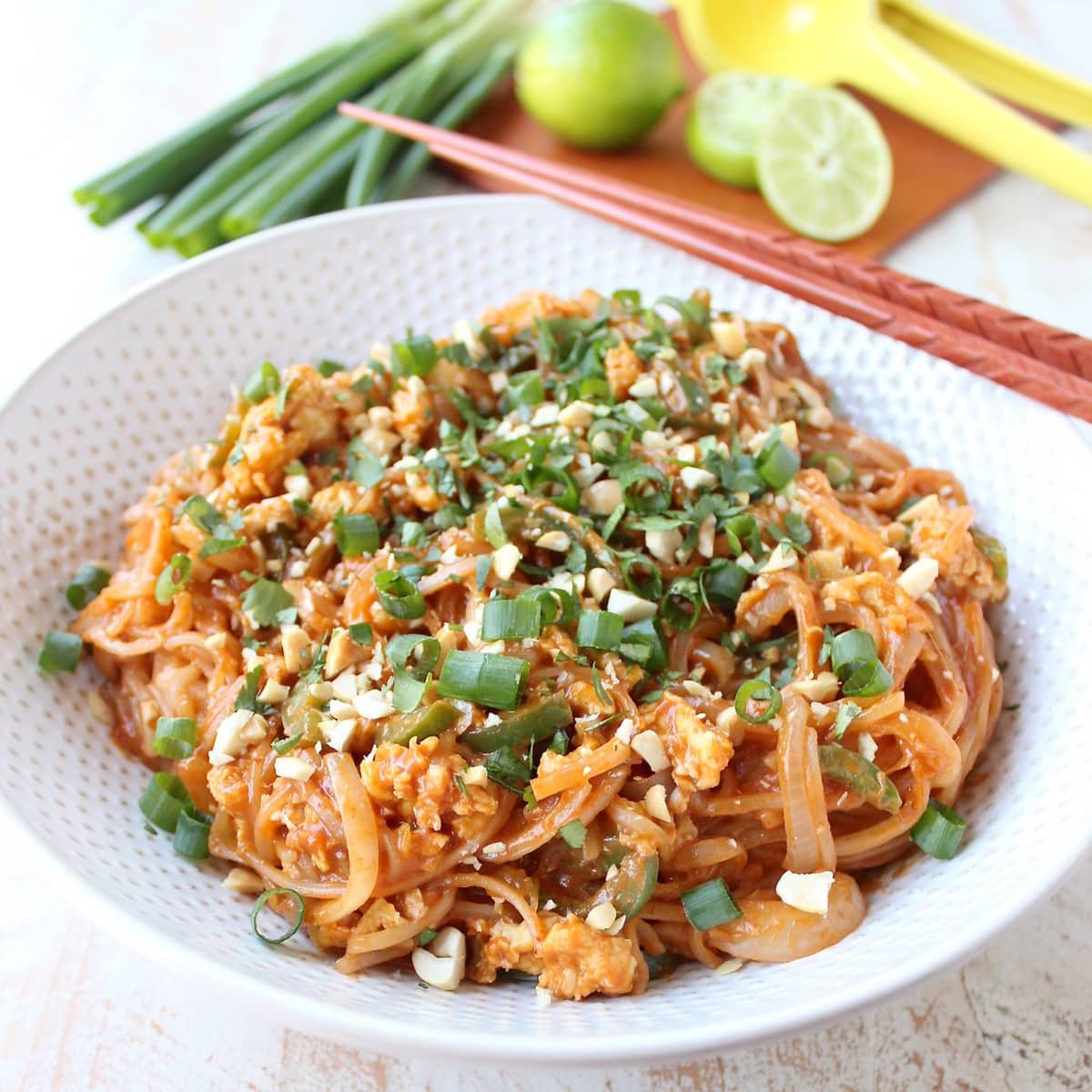 cooked pad thai in bowl topped with diced green onions, crushed peanuts and chopped cilantro
